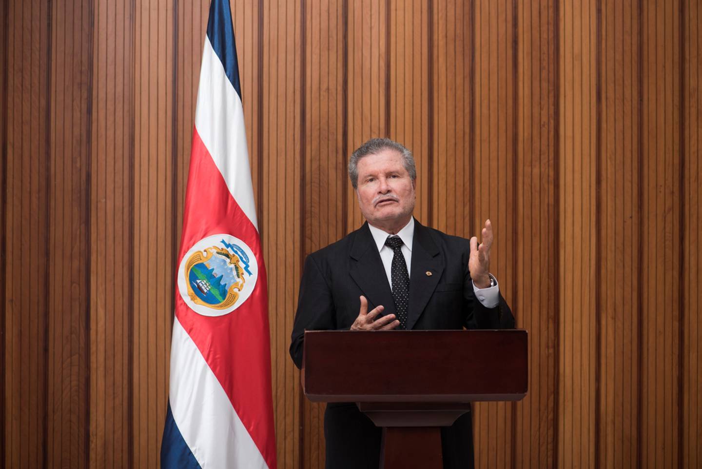 Un hombre en traje parado enfrente de una cortina roja

Descripción generada automáticamente con confianza media